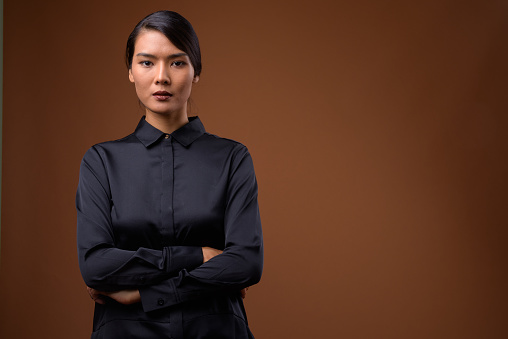 Studio shot of beautiful Asian businesswoman wearing black silk shirt against colored background horizontal shot