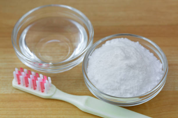 Closeup of baking soda powder next to vinegar, toothbrush on wooden background stock photo