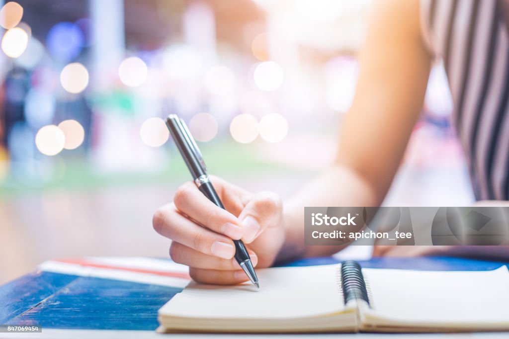 女性の手が木製の机の上にペンでノートに書きます。 - 手書き文字のロイヤリティフリーストックフォト