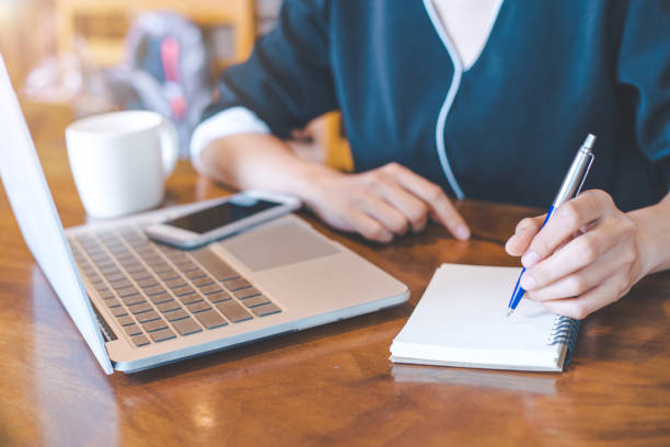 istock Business woman hand is working on a notebook computer and writing on a note pad with a pen. 847070466