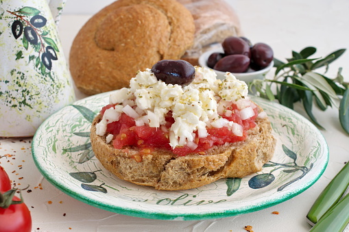 Dakos traditional greek appetizer on a traditional plate with ceramic olive oil jar, dry rye bread, olives and olive branch. Healthy eating concept. Mediterranean lifestyle