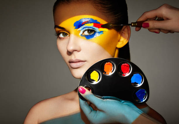 Makeup artist applies colorful makeup. Fashion model woman with colored face painted. Beauty art portrait of beautiful model with colorful abstract makeup