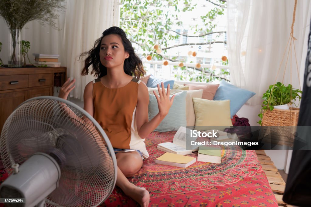 Too hot at home Sweating Asian girl cooling herself with big fan Heat - Temperature Stock Photo