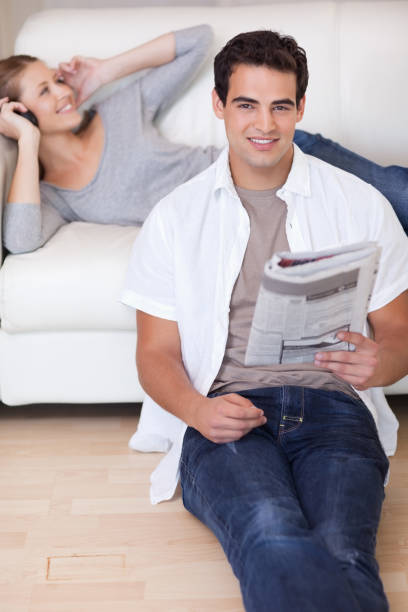 istock Man leaning against the sofa with newspaper while his girlfriend listens to music 847100806