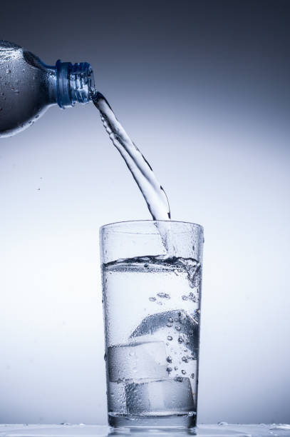 istock Pouring water from bottle into glass on blue background 847104226