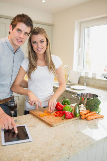 istock Woman chopping peppers with man typing on the tablet pc 847104876