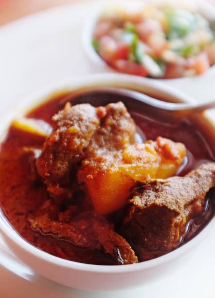 Serving of Indian lamb curry in bowl with sambal in background stock photo