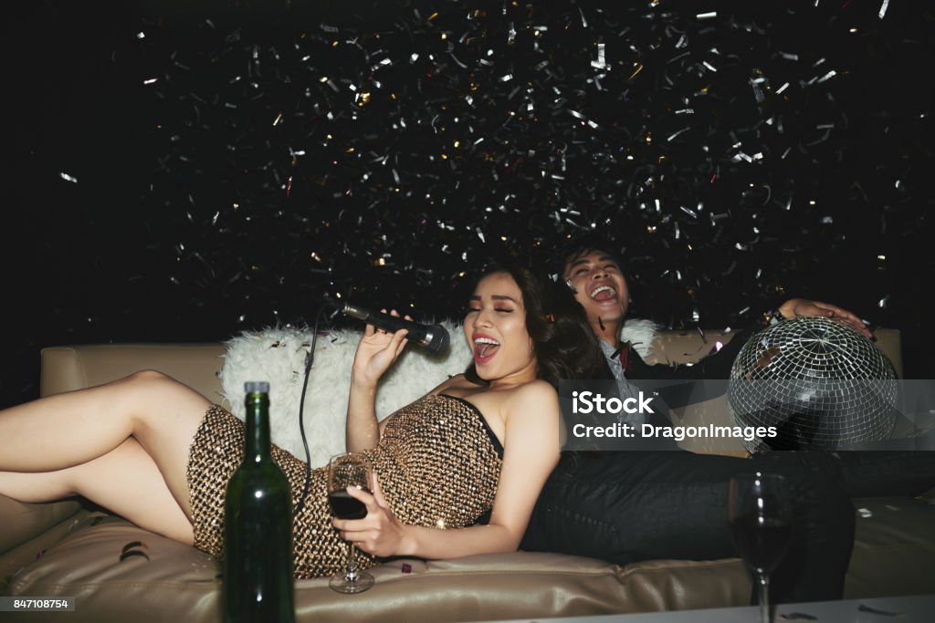 Partying couple Asian young couple lying on sofa and singing in microphone at the party Karaoke Stock Photo