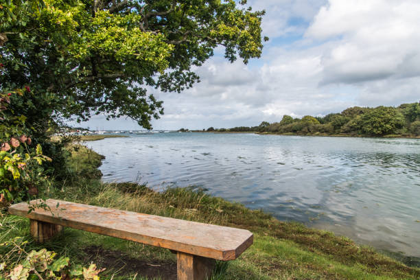 Shalfleet Quay bench seat Bench seat to sit and watch the waters of shalfleet quay and Newrtown Creek, clouds reflected in the water, distant views of yachts moored in the small natural harbour. newtown stock pictures, royalty-free photos & images