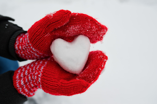 red female gloves hold a white heart from the snow. The concept of love and acceptance