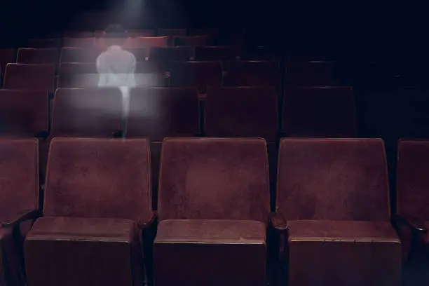 Photo of transparent ghost little girl appears between vintage seat in movie theater, horror film, halloween horror concept.