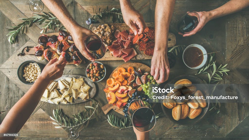 Top view of people having party, gathering, celebrating together Flat-lay of friends hands eating and drinking together. Top view of people having party, gathering, celebrating together at wooden rustic table set with different wine snacks and fingerfoods Appetizer Stock Photo