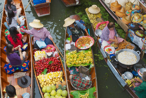 les femmes vendent des denrées alimentaires provenant des bateaux sur le marché flottant de damnoen saduak, thaïlande. - asia bangkok nautical vessel canal photos et images de collection