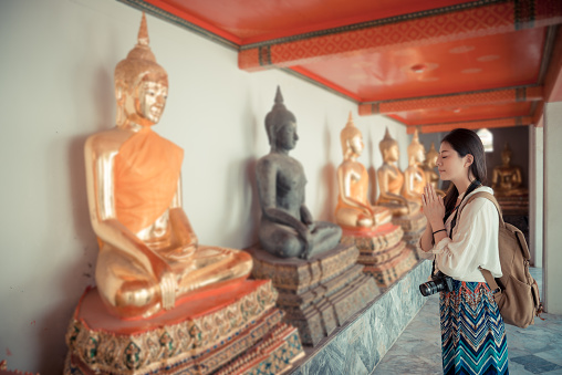 leisurely attractive woman travel in Bangkok, Thailand visiting famous wat pho temple and praying in front of buddha with vintage retro film color style.