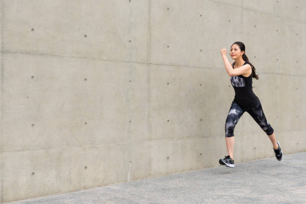 istock smiling female runner running on gray wall 847192128