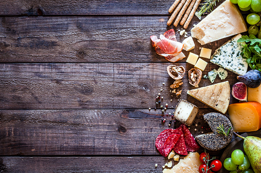 Top view of different types of cheeses and cold meat assortment arranged at the right border of a rustic wooden table leaving useful copy space for text and/or logo. Some fruits like figs and grape and some nuts complete the composition. DSRL studio photo taken with Canon EOS 5D Mk II and Canon EF 100mm f/2.8L Macro IS USM