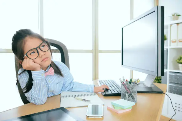 cute beautiful little girl children play as office worker sitting on working desk using business computer feeling boring.