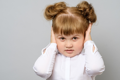 Disappointed little girl covering her ears isolated