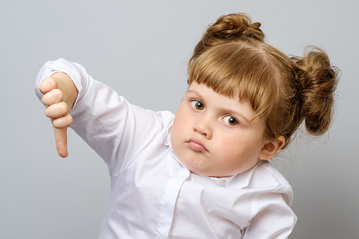 Unhappy little girl showing thumb down gesture isolated