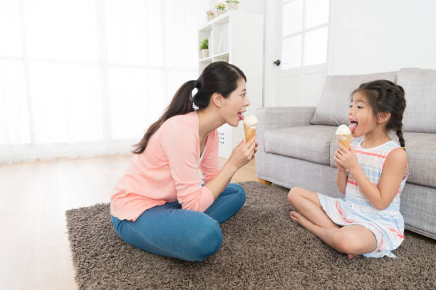 happy pretty mother sitting on living room floor happy pretty mother sitting on living room floor with lovely beauty daughter licking ice cream enjoying summer season at home. asian little chinese girls eating ice cream stock pictures, royalty-free photos & images