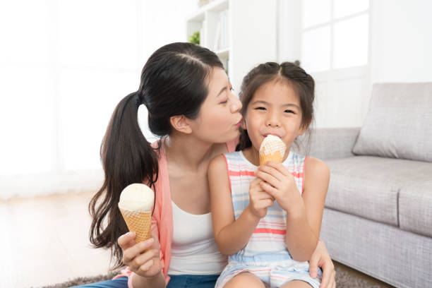 young mother kissing her lovely little daughter beautiful young mother kissing her lovely little daughter when girl looking at camera eating ice cream enjoying summer day feeling cheerful. asian little chinese girls eating ice cream stock pictures, royalty-free photos & images