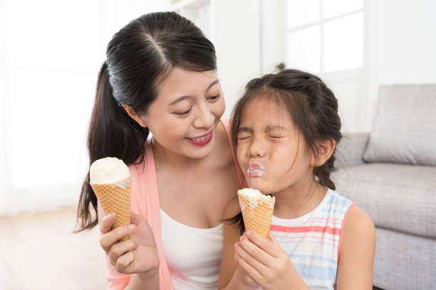 beautiful mother looking at pretty little daughter smiling beautiful mother looking at pretty little daughter eating ice cream feeling happiness and enjoying summer season at home together. asian little chinese girls eating ice cream stock pictures, royalty-free photos & images