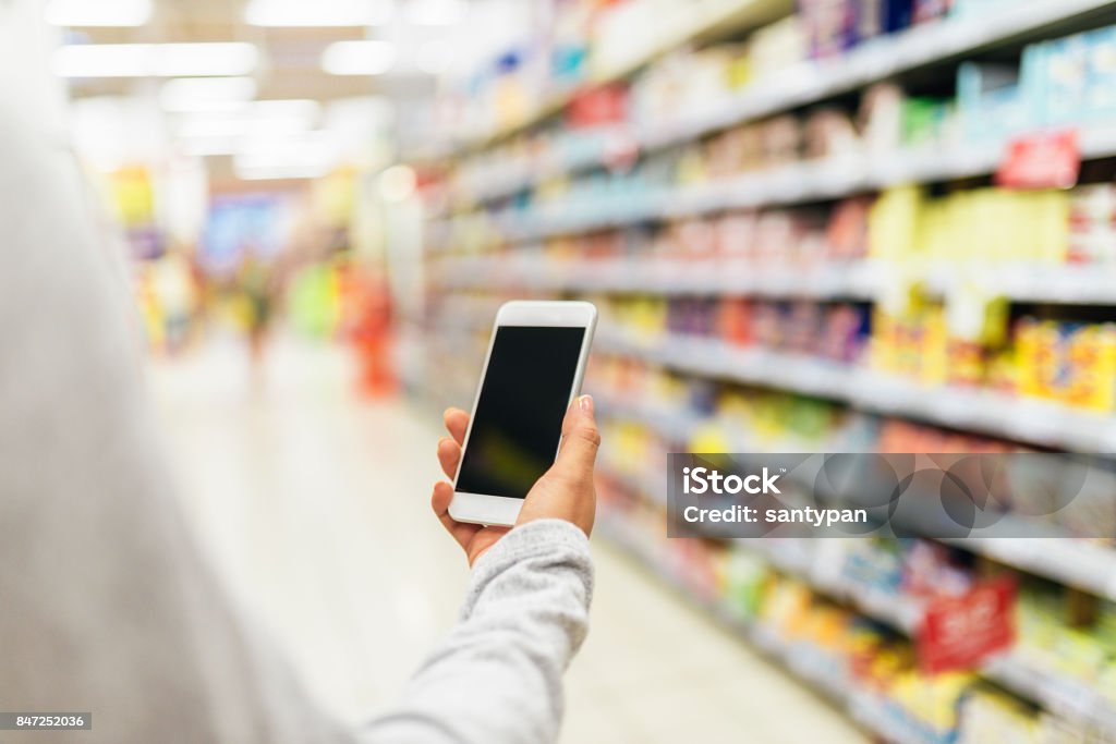 Feche de mulher usando seu celular no supermercado. - Foto de stock de Supermercado royalty-free