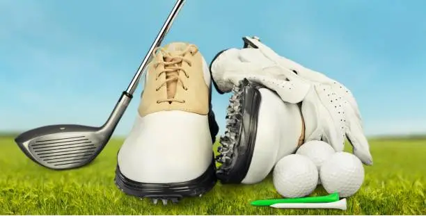 Pair of golfing shoes and a golf club on green grass background