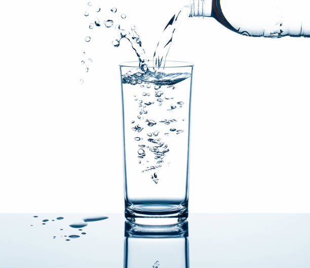 istock Drinking water pouring from bottle into glass with air bubbles and water splash with reflection on glass table isolated on white background 847284458