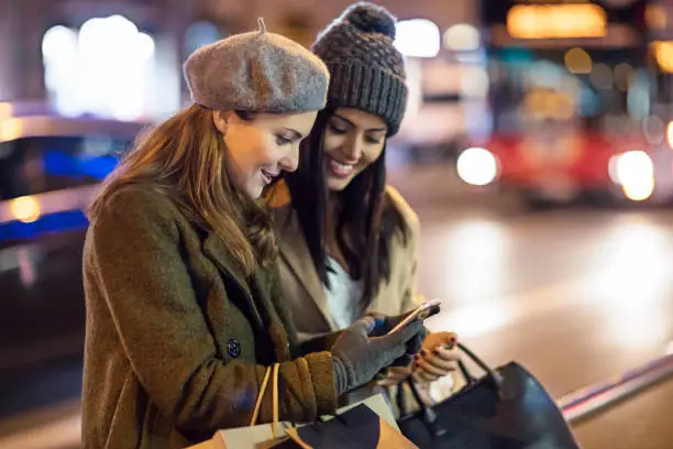 Photo of Beautiful women checking mobile phone in the street after shopping in the city at night