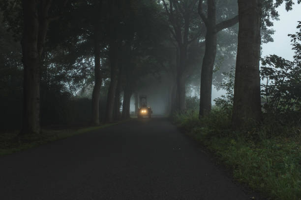 istock Misty country road with tractor and illuminating headlights. 847296844