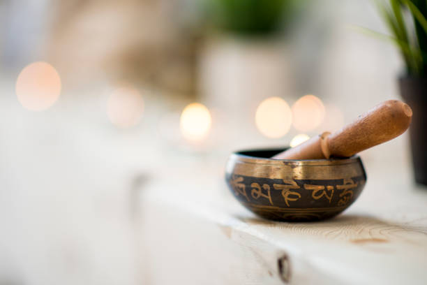 Singing Bowl A small singing bowl rests on an untreated wood bench, behind it are candles and plants. It is the backdrop of a yoga studio, and is there for relaxation and meditation. gong stock pictures, royalty-free photos & images
