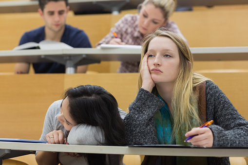 Demotivated students sitting in a lecture hall with one girl napping in college