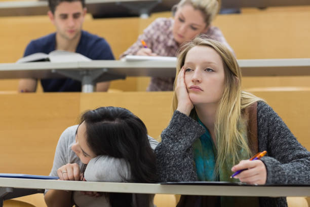 Demotivated students in a lecture hall Demotivated students sitting in a lecture hall with one girl napping in college male college student sleeping through lecture stock pictures, royalty-free photos & images