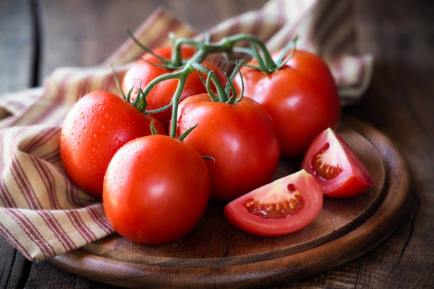 Tomatoes on the vine Fresh red ripe tomatoes on the vine on a dark rustic cutting board tomato stock pictures, royalty-free photos & images