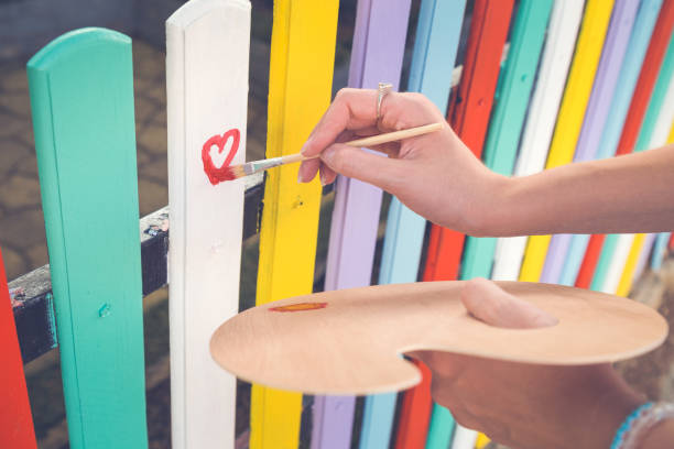 woman draw heart on colorful fence with painting brush - brushing human hand paintbrush artist imagens e fotografias de stock