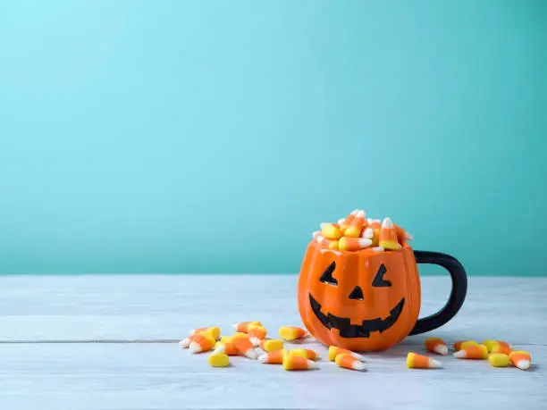 Halloween celebration concept with candy corn and jack o lantern cup on wooden table.