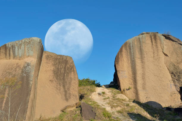 Composite of big rocks against the moon on a clear ble sky