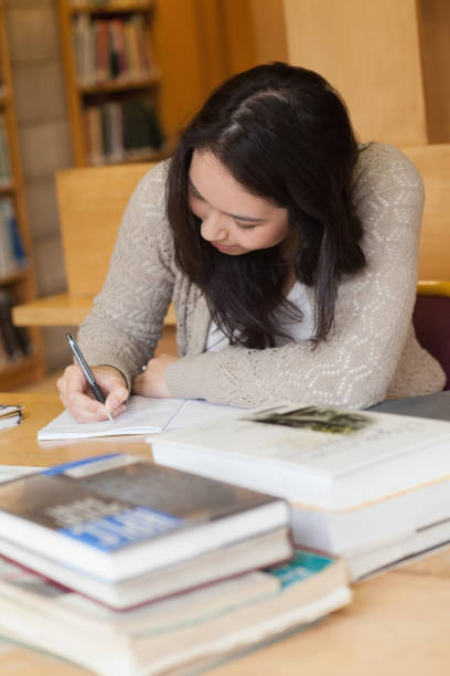 istock Student sitting in a library at a desk and writing 847354144