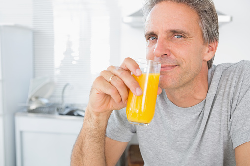 Happy man drinking orange juice in kitchen looking at camera