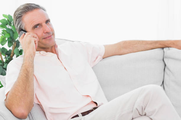 istock Man on his couch on the phone smiling at camera 847371826