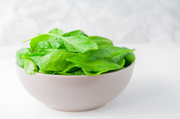 istock Fresh spinach leaves with water drops in ceramic bowl on thw white wooden background. Selective focus. Space for text 847371940