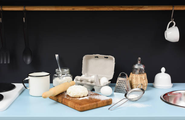istock Kitchen table in process of making homemade cookies. Raw dough, rolling pin, sieve, eggs, flour and kitchen utencils on black and blue background 847379810
