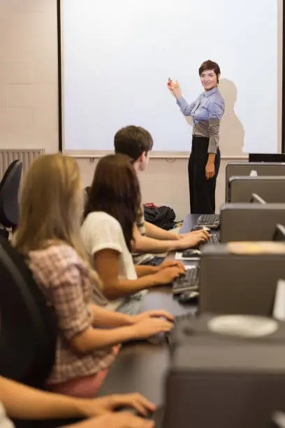 Photo of Computer class looking at teacher pointing on projection screen