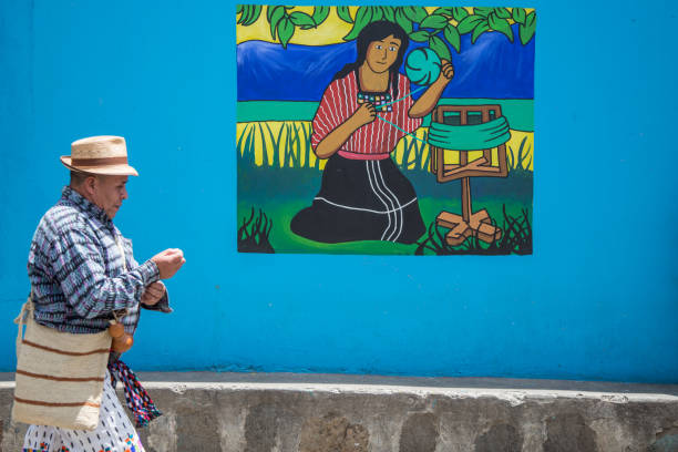 One Indigenous Guatemalan man, wearing the traditional colorful clothings,  walking next to a colorful mural, San Juan del lago.