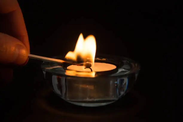 Hand lighting tea light candle in glass holder in the dark