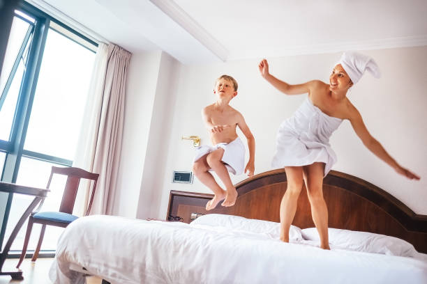 mère et fils sautent sur le lit dans la chambre d’hôtel de luxe - hotel room hotel luxury mattress photos et images de collection