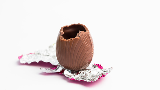 Easter egg unwrapped in pink foil with bite taken out on white background