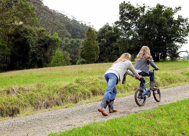 mütter schieben tochter bergauf auf ihrem fahrrad - yarramalong stock-fotos und bilder