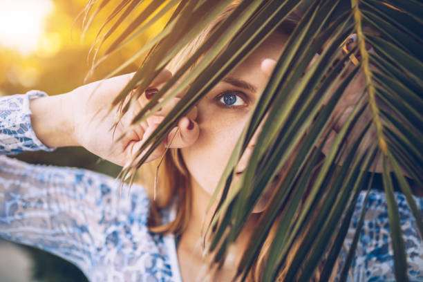istock Beautiful blue-eyed woman looking through palm tree leaf 847526702